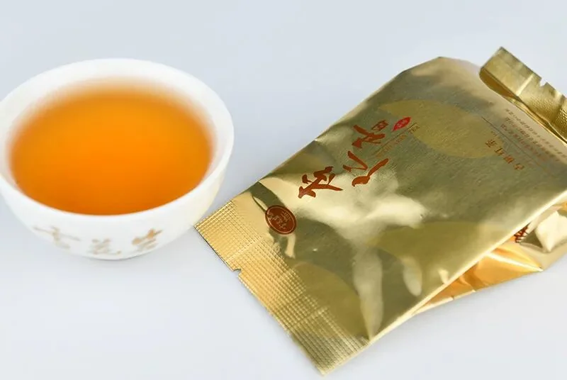 Xuehuayan Snow Flower Rock almond aroma wild ancient tree black tea — gold foil packet with brewed amber tea liquor